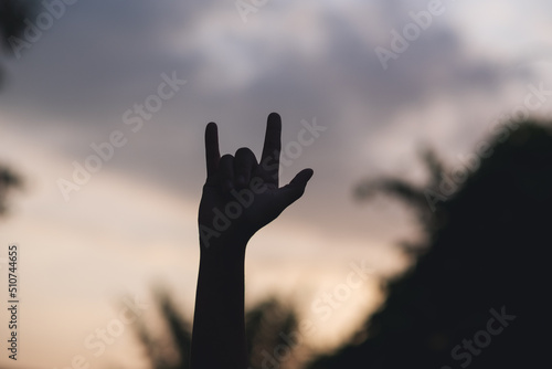 Silhouette of hands making love hand sign with blurred sunset sky background