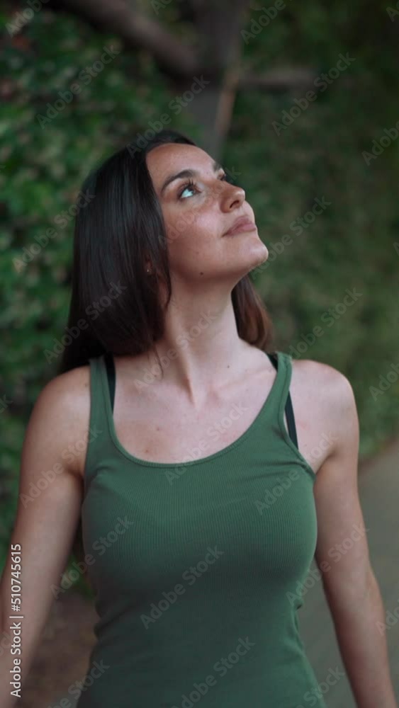 VERTICAL VIDEO: Girl in green top walks through an arch covered with green plants along the road. Young woman smiling walks along the sidewalk looking at wall overgrown with green leaves VERTICAL VIDEO: Girl in green top walks through an arch covered with green plants along the road. Young woman smiling walks along the sidewalk looking at wall overgrown with green leaves