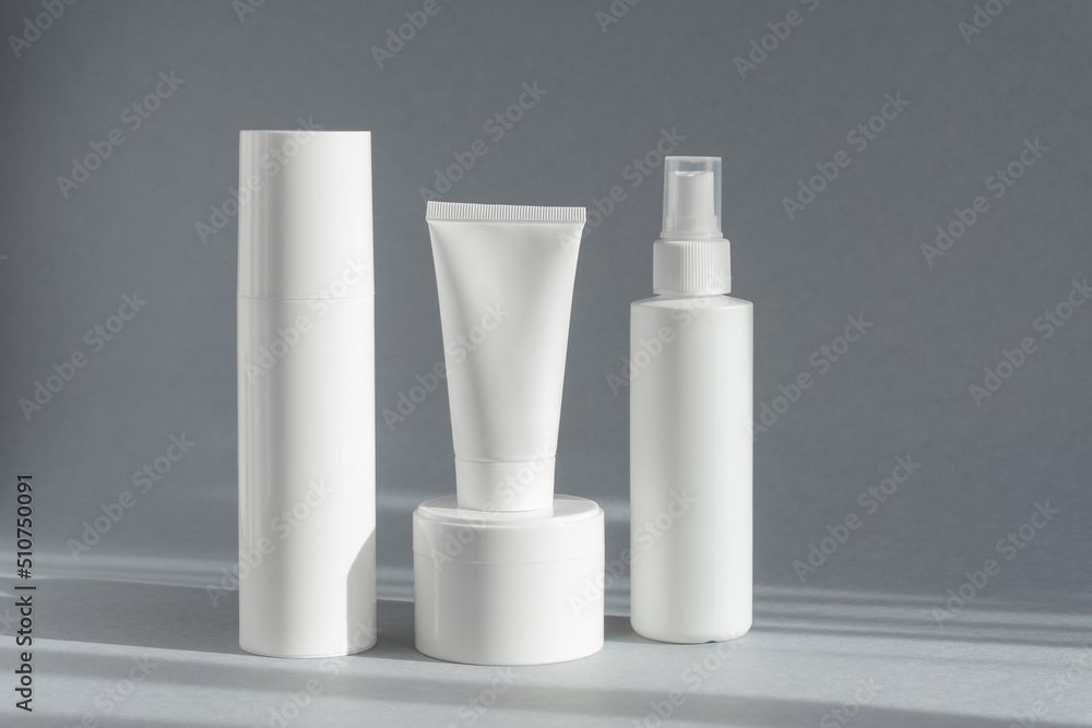 Foam for washing in an aerosol, lotion with spray cap, tube of moisturizer, jar of cosmetic ointment on gray background, in rays of sunlight. Mockup of white unmarked bottles. Concept of body care Foam for washing in an aerosol, lotion with spray cap, tube of moisturizer, jar of cosmetic ointment on gray background, in rays of sunlight. Mockup of white unmarked bottles. Concept of body care