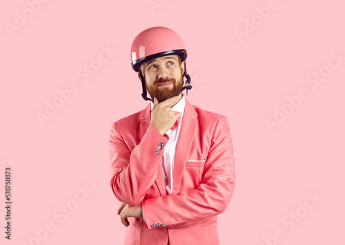 Photography Funny young Caucasian man in pink helmet and suit isolated on studio background think or ponder