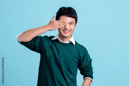 Young handsome Asian man wearing casual clothes over light blue background. He covering his eyes