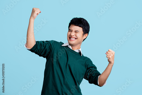 Portrait of a cheerful young Asian man in casual clothes. He raised his fist with a happy smile on his face as a gesture of celebration.