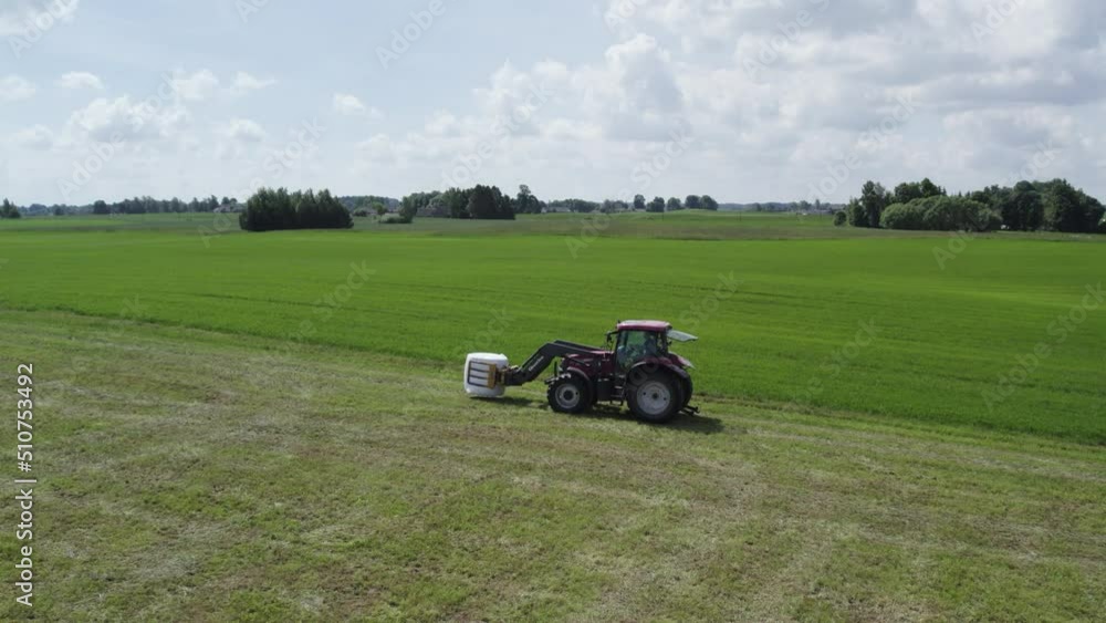 Tractor loads bales from the field onto the trailer. Tractor loads bales from the field onto the trailer.