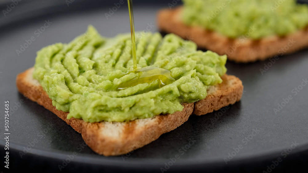 Cooking avocado toast. Pour oil over mashed avocado on toasted bread. Vegan food concept Cooking avocado toast. Pour oil over mashed avocado on toasted bread. Vegan food concept