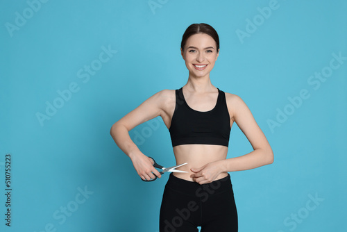 Slim young woman with scissors on light blue background, space for text. Weight loss surgery © New Africa