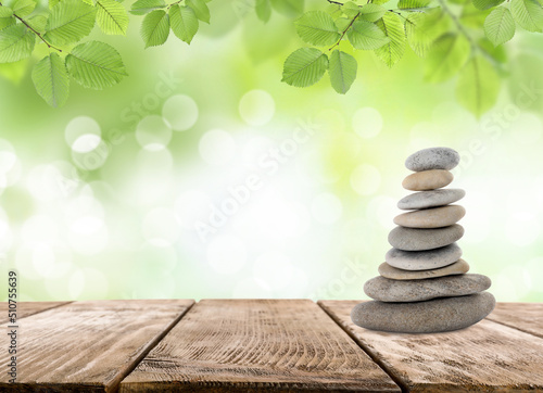 Stacked stones on wooden table under green leaves against blurred background, space for text. Zen concept