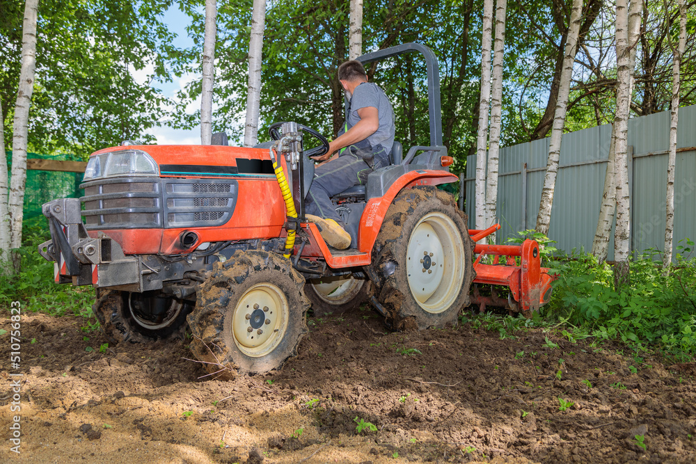 A farmer on a mini tractor loosens the soil for the lawn. Land cultivation, surface leveling. A farmer on a mini tractor loosens the soil for the lawn. Land cultivation, surface leveling.