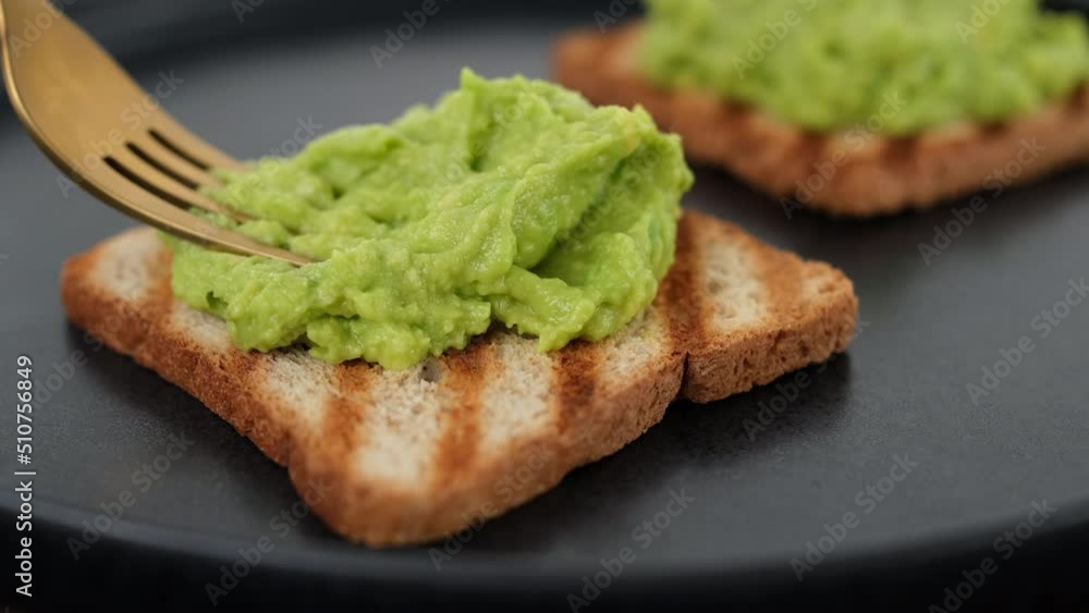 Cooking avocado toast. Hands with fork spreading mashed avocado on toasted bread. Vegan food concept Cooking avocado toast. Hands with fork spreading mashed avocado on toasted bread. Vegan food concept