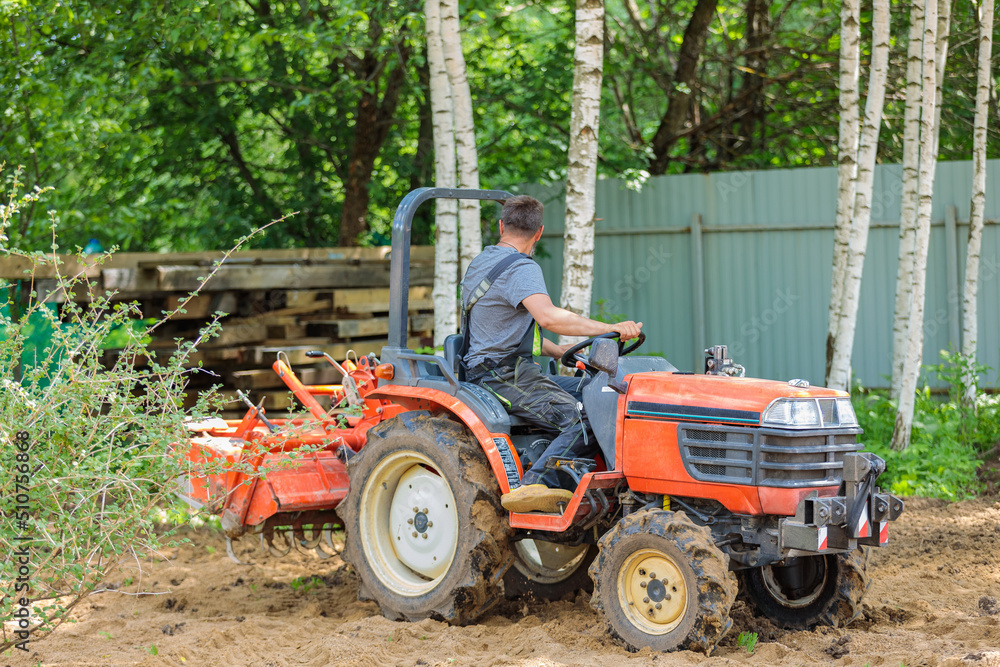 A farmer on a mini tractor loosens the soil for the lawn. Land cultivation, surface leveling. A farmer on a mini tractor loosens the soil for the lawn. Land cultivation, surface leveling.