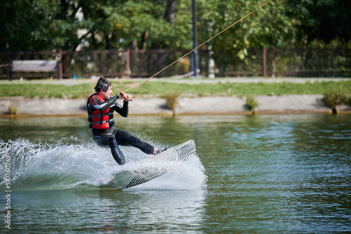 Wakeboarder surfing on lake. Young man surfer having fun wakeboarding in the cable park. Water sport, outdoor activity concept.