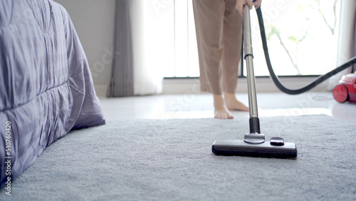 Asian young housekeeper using vacuum machine to clean a dirty floor in the living room.