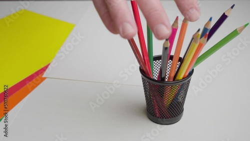 The artist takes a colored pencil from a stand. Close-up hand takes a black pencil from a set of pencils.