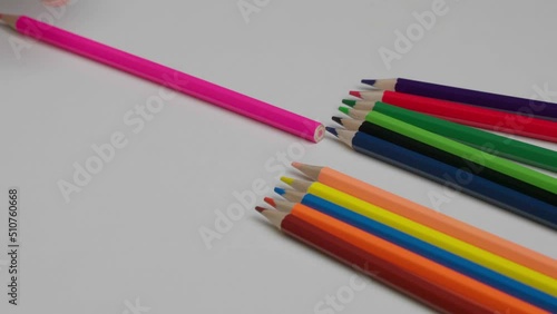Lots of colored pencils on a white table. The artist chooses a pink pencil from a group of colored pencils.