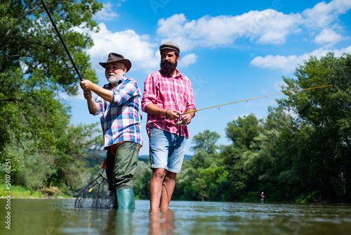 Father and mature son fisherman fishing with a fishing rod on river.
