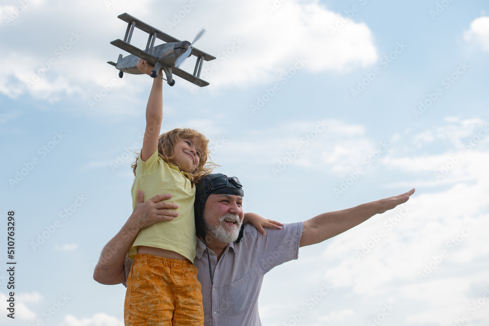 Amazed grandson child and grandfather having fun with plane outdoor on sky background with copy space. Child dreams of flying, happy childhood with grand dad.
