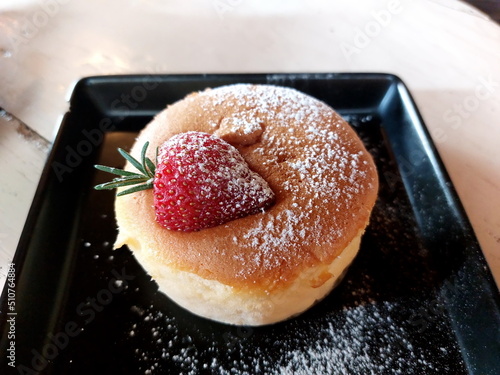 Japanese cotton cheesecake with strawberry and icing sugar on black plate.