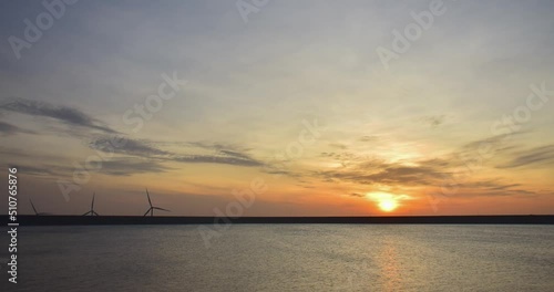 The sun rises over the water between the wind turbines in operation.