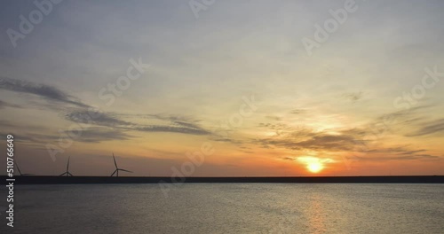 The sun rises over the water between the wind turbines in operation.