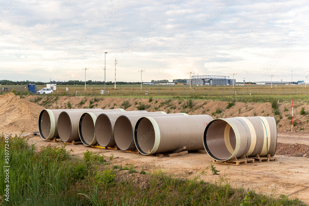 Stack of big frp composite fiberglass plastic sewage pipes at warehouse construction site near Leipzig Halle airport against blue sky background. Highway road construction infrastructure earthworks Stack of big frp composite fiberglass plastic sewage pipes at warehouse construction site near Leipzig Halle airport against blue sky background. Highway road construction infrastructure earthworks