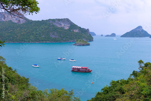 Thailand - Angthong Islands National Marine Park, view of the sea and hills from Koh Mae Koh island. Tourist boats on calm turquoise sea. Lush foliage surrounds.
