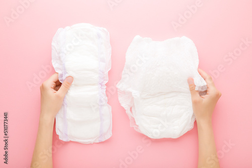Photos Young adult woman hands holding white big size sanitary towel and diaper pant on pastel pink background