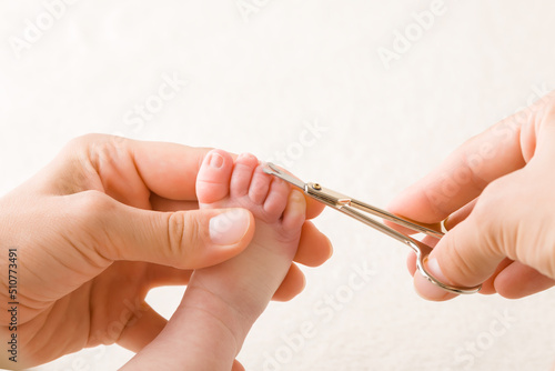 Young adult mother hands cutting newborn toe nails with scissors. Closeup. Point of view shot.