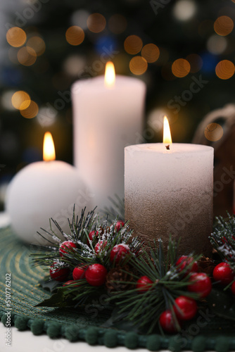 Beautiful burning candles and Christmas decor on white table against festive lights