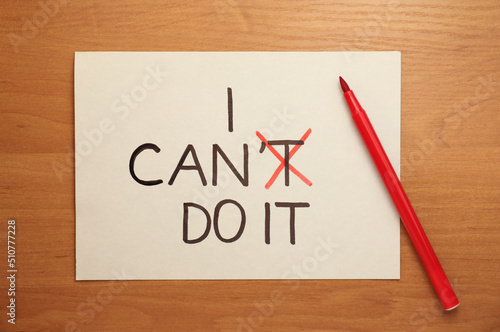 Phrase I Can Do It with crossed letter T in card and felt tip pen on wooden table, top view