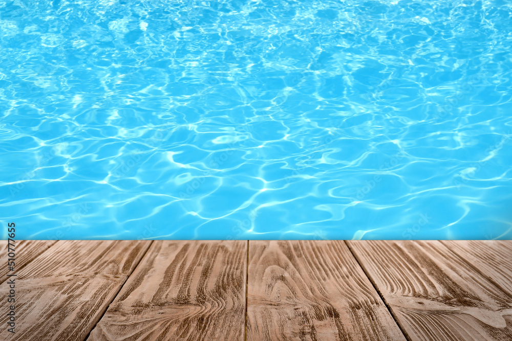 Empty wooden surface near swimming pool with clear water. Space for design