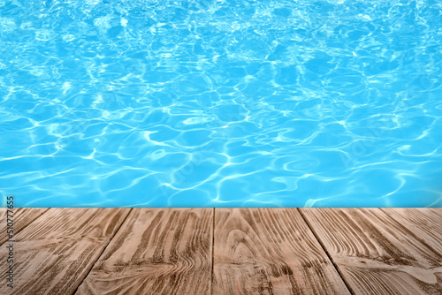 Empty wooden surface near swimming pool with clear water. Space for design