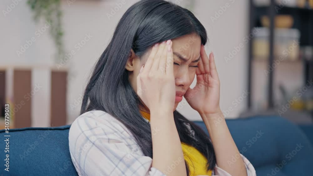 Sad Asian woman suffering from migraine, massaging temples, disease symptom Sad Asian woman suffering from migraine, massaging temples, disease symptom