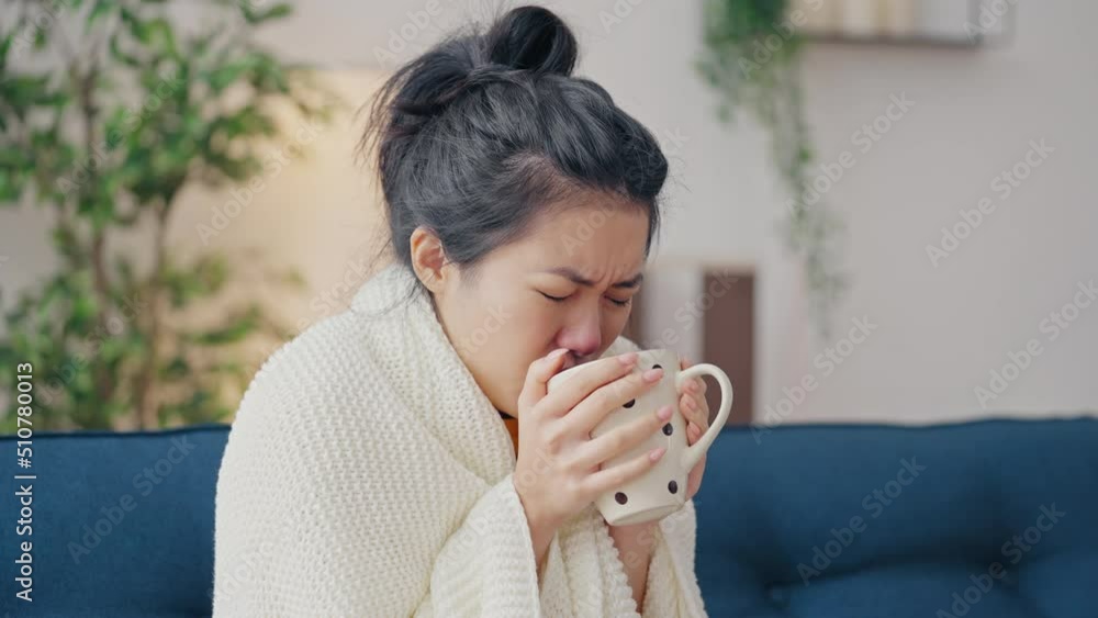 Woman wrapped in blanket coughing and drinking tea, suffering from covid-19 Woman wrapped in blanket coughing and drinking tea, suffering from covid-19