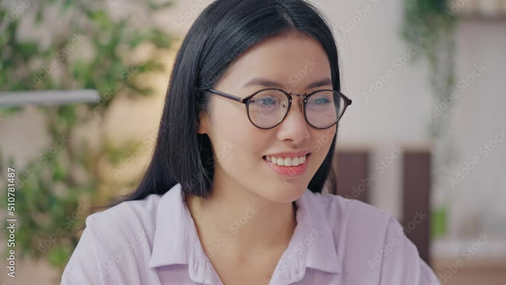 Smiling Asian woman in eyeglasses reading e-mail with great news on laptop Smiling Asian woman in eyeglasses reading e-mail with great news on laptop