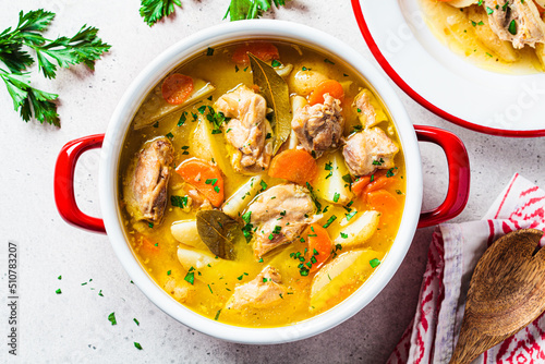 Chicken stew with potatoes and carrots in red saucepan. Chicken soup with vegetables and herbs. Comfort food recipe.