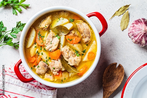 Chicken stew with potatoes and carrots in red saucepan. Chicken soup with vegetables and herbs. Comfort food recipe.