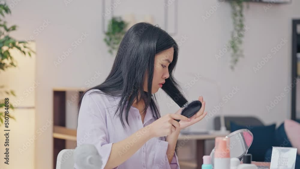 Young Asian female combing weak hair and looking at brush, split ends problem Young Asian female combing weak hair and looking at brush, split ends problem