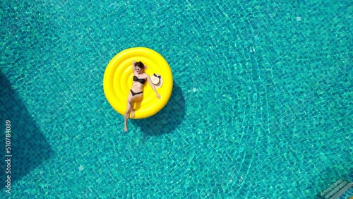 Beautiful young asian woman with yellow inflatable ring relaxing in swimming pool. top view
