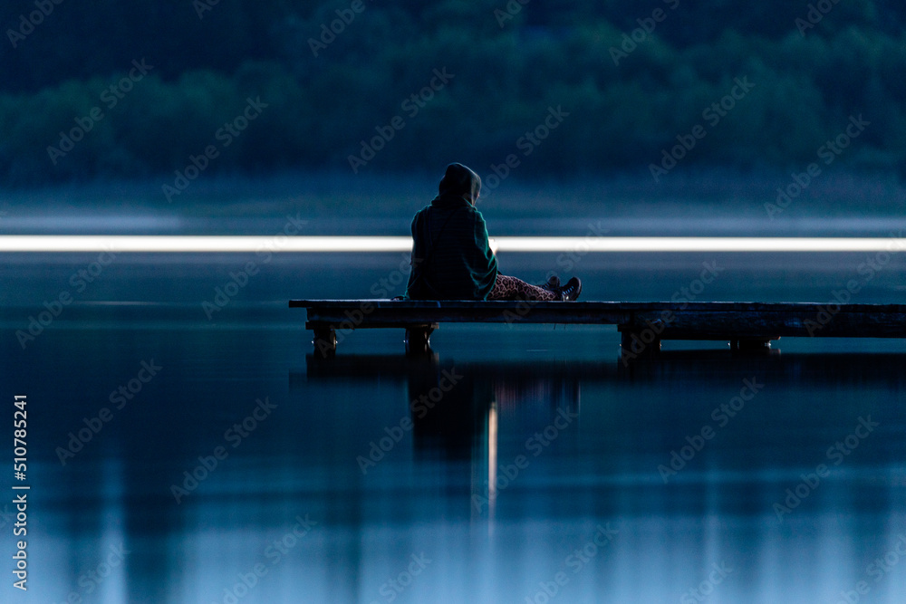Naklejka premium dziewczyna siedząca na molo nocą
