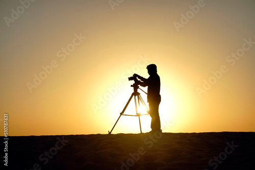 Unidentifiable photographer with tripod and camera working on sand dune in Dubai, UAE.