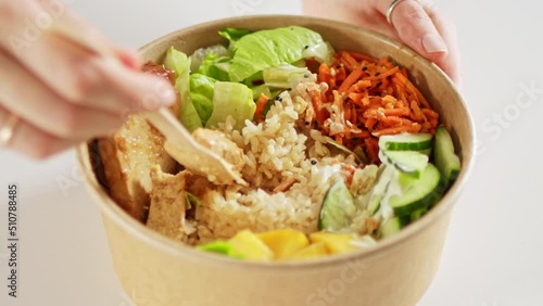 Hands taking food from asian poke vegan bowl with rice, avocado, tofu and salad. Healthy vegetarian delivery meal. photo