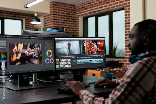 African american creative digital video editor sitting at desk while improving recorded footage visual quality. Professional post production videographer editing graphic content using specialized
