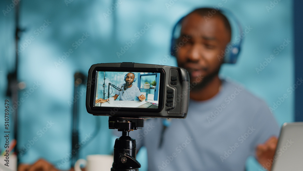 Close up of camera screen recording blogger with headphones for vlog channel. Vlogger using modern equipment and tripod to film video for online podcast. Man filming for social media