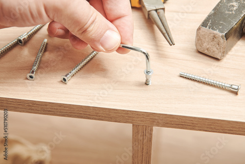 The furniture assembler tightens the bolt fixing into the furniture made of particle board with a hex wrench. Furniture assembly process. DIY Assembling. Close up view photo