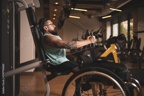 A middle-aged person in a wheelchair training in a gym, working his pecs. Sports overcoming concept.
