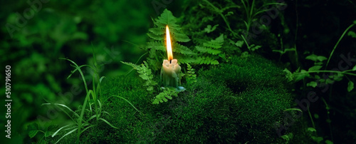 Obraz na plátně burning candle on moss, dark green blurred natural background