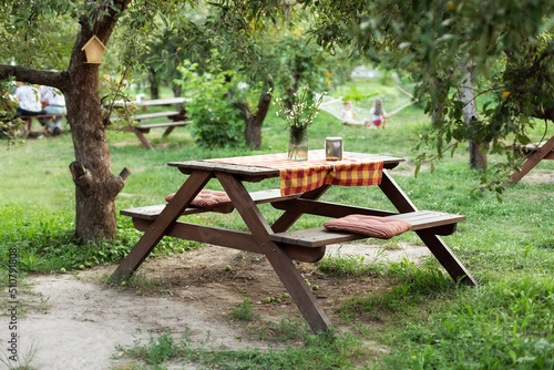 Beautiful picnic area with wooden table in summer garden. Resting place on park. Picnic place in Orchard at backyard. Wooden picnic table with benches on beautiful grass lawn in quiet place. Bench