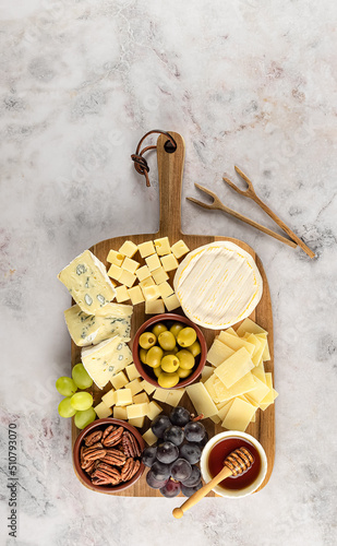 Party cheese board with a variety of cheese, grape, nuts, olives, and honey on a kitchen plate
