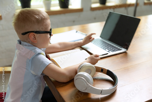 Happy school age kid sitting at home and doing homework at home interior, indoors. Online education, childhood, people, remote learning and school concept.