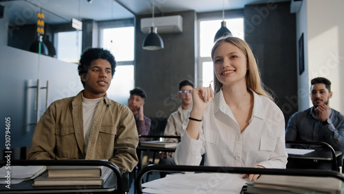 Diverse students classmates attentively listening to interesting lecture enthusiasm in classroom young caucasian girl raising hand knows answer answers question higher education concept in college