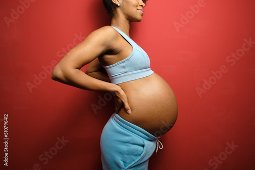 Detail of sporty pregnant woman belly on red wall background. photo